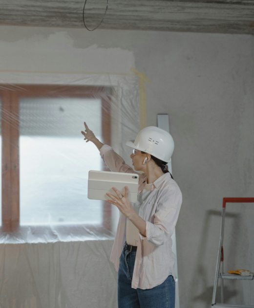 Woman in hard hat using tablet to oversee home renovation in a partially completed room.